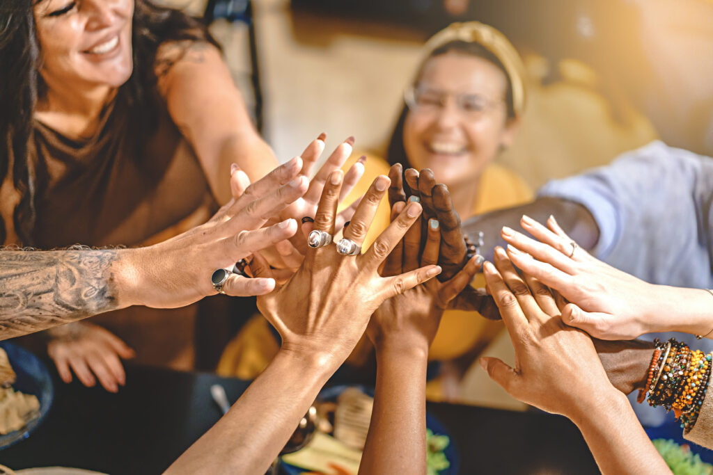 Diverse group of friends joining hands in a high-five to celebrate connection, teamwork, and global wellness impact.