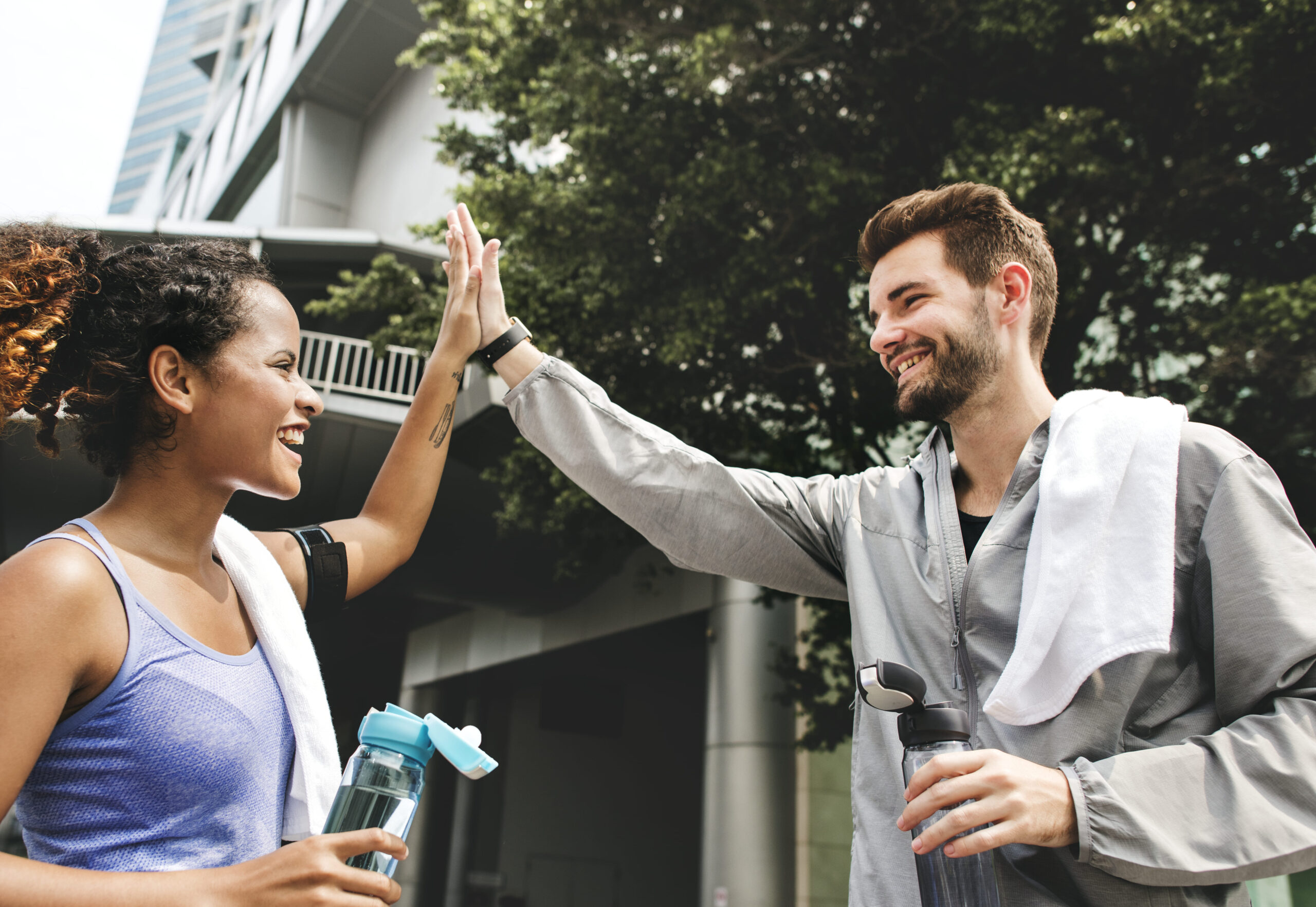 Smiling coworkers giving a high five after a workout, holding water bottles and wearing athletic gear, symbolizing teamwork and workplace wellness success.