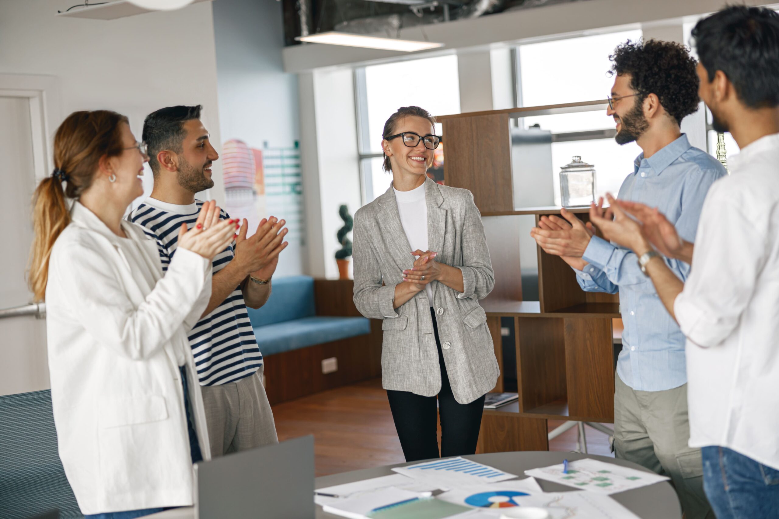 A diverse group of colleagues applauding and smiling as they recognize an HR professional during a workplace celebration.