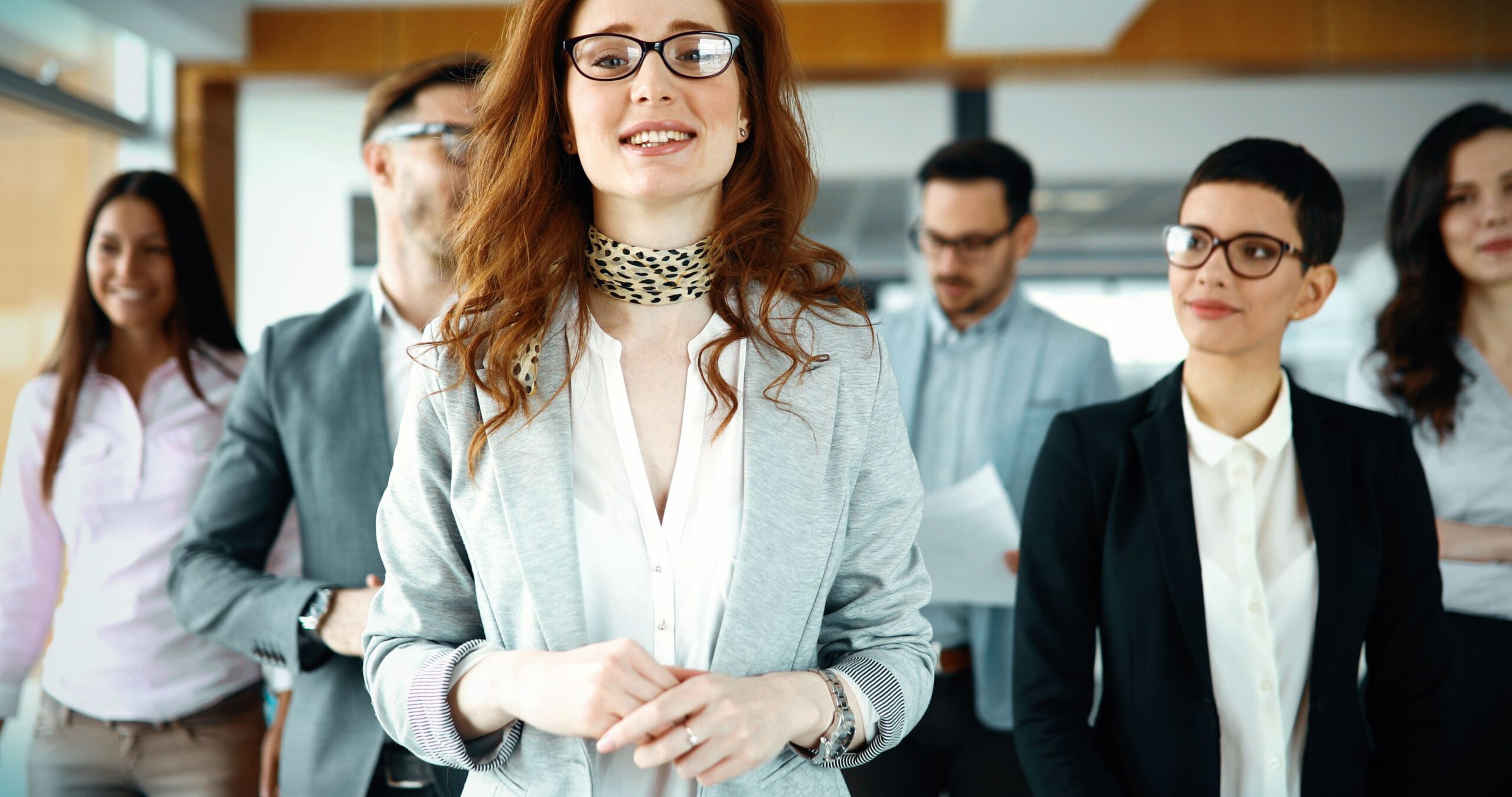Confident female business leader standing at the forefront with her smiling team in the background, symbolizing collaboration and success in a corporate setting.