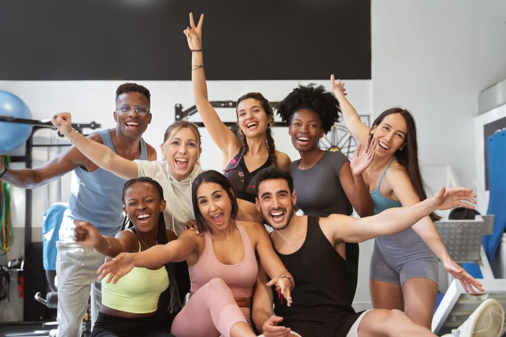 Diverse group of employees smiling and celebrating wellness together in a fitness setting, symbolizing workplace recognition, connection, and engagement.