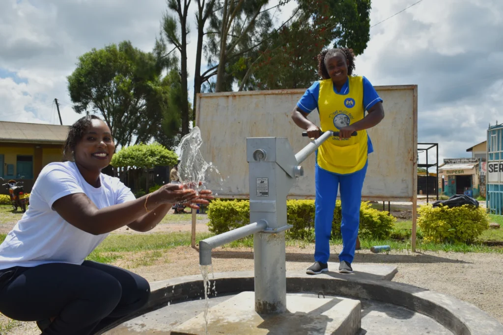 Two women in Kenya pump and collect clean water from a community well, smiling as they celebrate access to safe water provided through The Water Project.