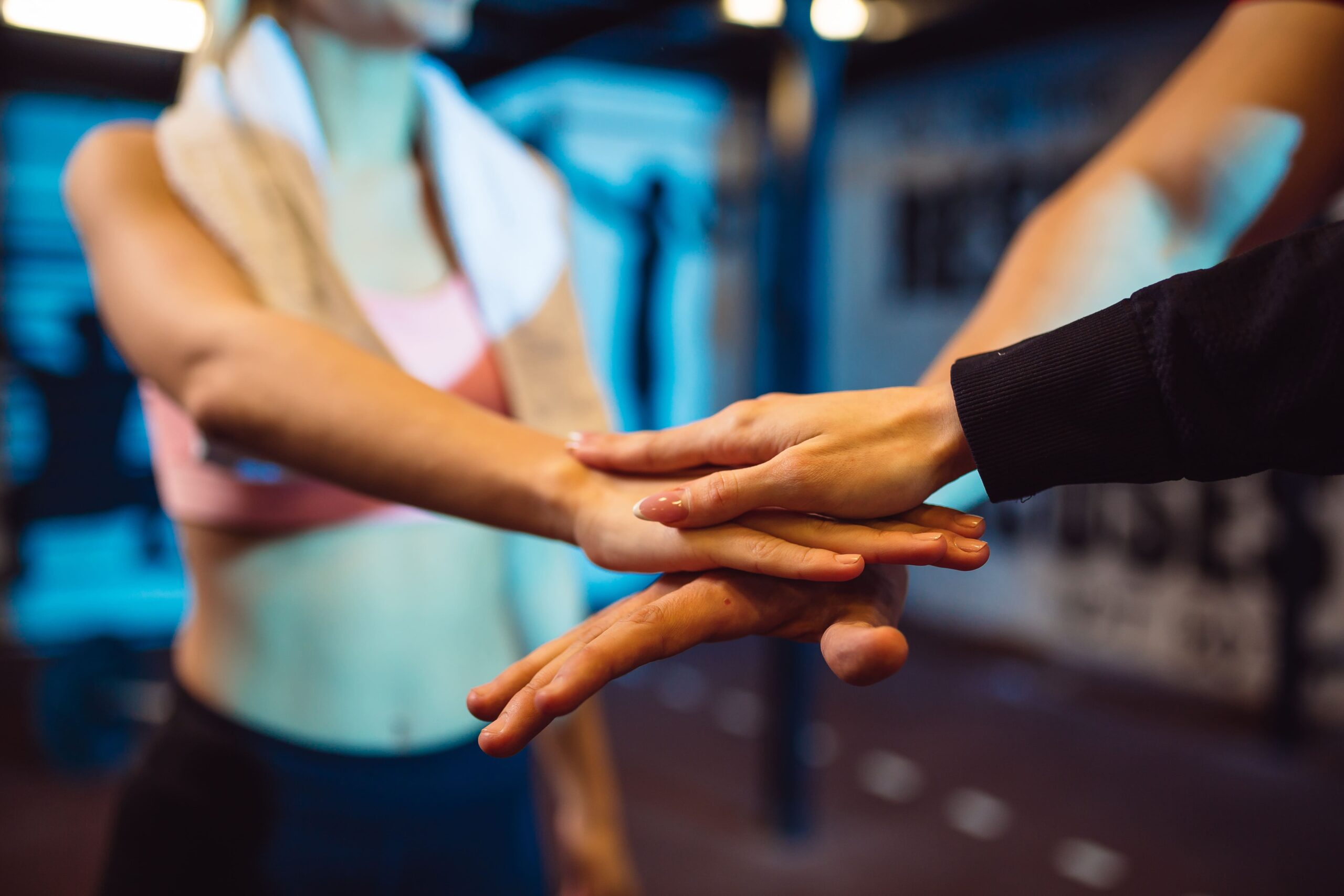 Close-up of a group of coworkers stacking hands in a gym, symbolizing teamwork, wellness, and mutual support in the workplace.