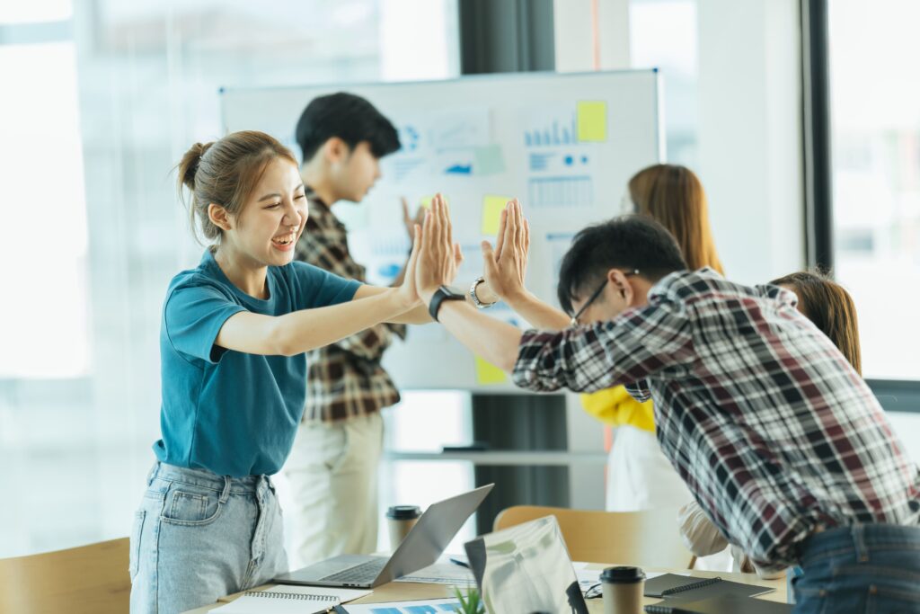 Coworkers smiling and giving each other a high five in an office, symbolizing teamwork, employee engagement, and positive workplace wellness outcomes.