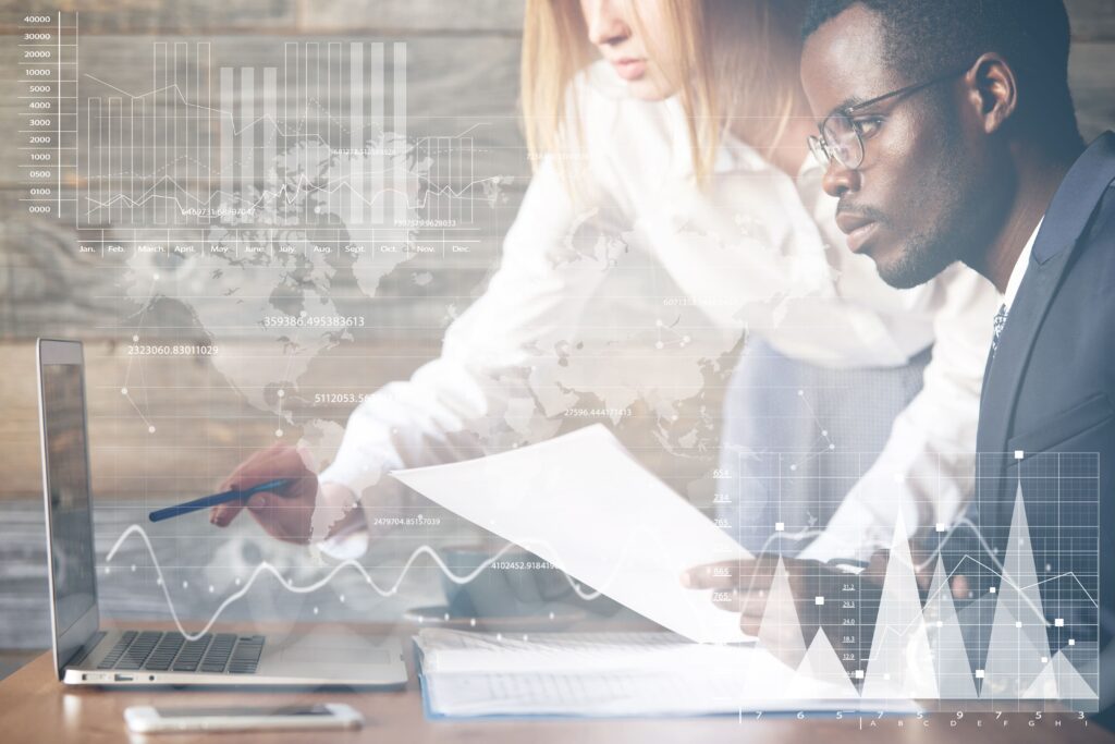 Two business professionals reviewing reports and digital analytics dashboards on a laptop, representing employer evaluation of wellness program performance, data integration, and the shift from fragmented multi-vendor solutions to unified wellbeing platforms.