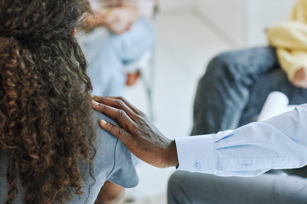 A supportive hand rests on a woman's shoulder during a group discussion, symbolizing mental health support, empathy, and early intervention in workplace wellbeing.