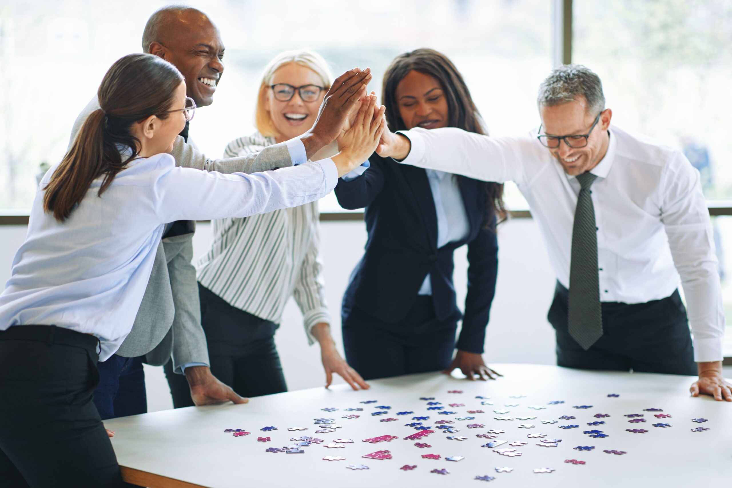 Business team celebrating progress together around a table, representing outcomes-based wellbeing, collaboration, and sustainable performance at work.