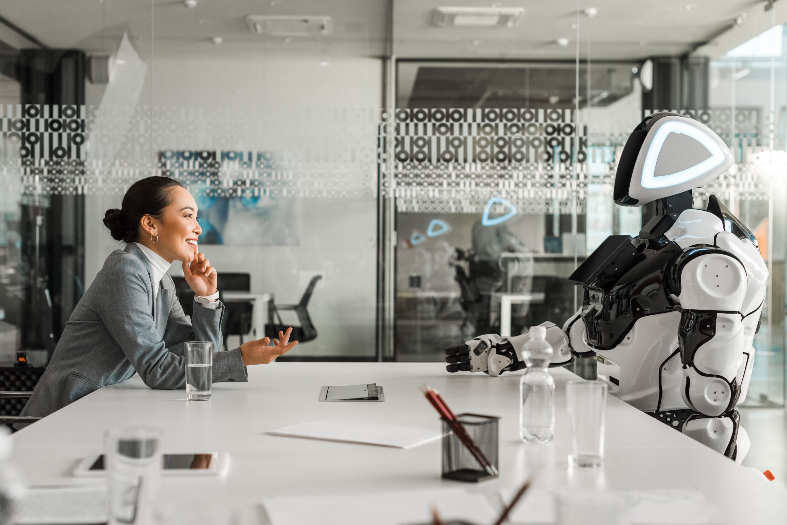 HR leader speaking with an AI-powered system at a conference table, illustrating how artificial intelligence supports decision-making and frees HR to focus on people and culture.
