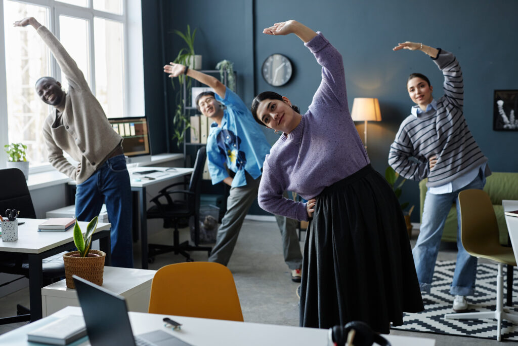Employees stretching together during a workplace wellness break, illustrating how daily engagement activities support long-term workforce health outcomes and prevention.