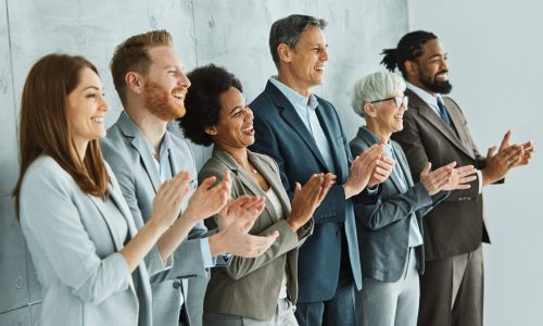 A diverse group of professionals standing in a row clapping and smiling, symbolizing employee recognition, appreciation, and positive workplace culture.