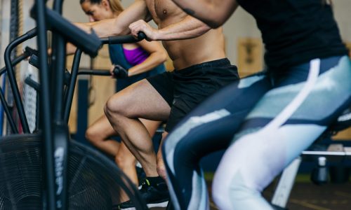 Employees participating in a cardio-focused workout on air bikes, highlighting the role of physical activity in improving cardio-metabolic health and reducing employer healthcare costs.