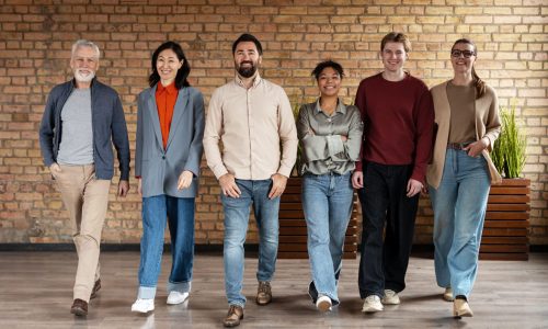 A diverse group of six smiling professionals walks confidently together inside a modern office space, symbolizing teamwork, culture, and strong people operations.