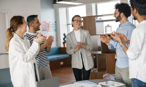 A diverse group of colleagues applauding and smiling as they recognize an HR professional during a workplace celebration.