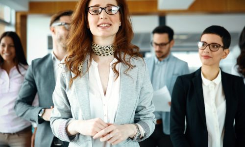 Confident female business leader standing at the forefront with her smiling team in the background, symbolizing collaboration and success in a corporate setting.