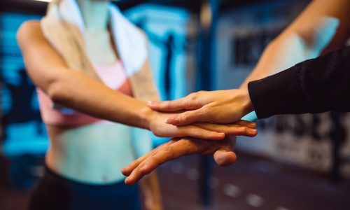 Close-up of a group of coworkers stacking hands in a gym, symbolizing teamwork, wellness, and mutual support in the workplace.