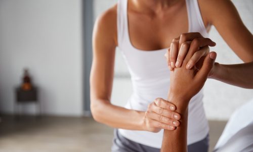 A wellness practitioner helping a person stretch their arm, illustrating musculoskeletal (MSK) prevention and early intervention strategies for reducing employer healthcare claims.