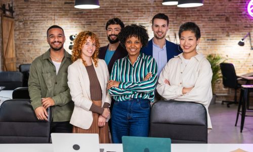 Diverse group of smiling startup team members standing confidently together in a modern open office, representing strong company culture and collaboration.