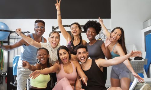 Diverse group of employees smiling and celebrating wellness together in a fitness setting, symbolizing workplace recognition, connection, and engagement.