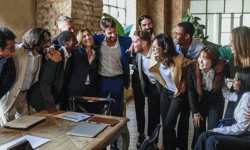 A diverse team of colleagues standing close together, smiling and supporting one another in an office setting—symbolizing strong team connection and the cultural value of employee retention in startups.