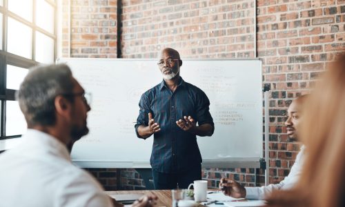 A founder-style leader stands in front of a whiteboard presenting to a team, modeling strong communication and a culture of openness and alignment.