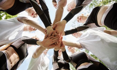 A team standing in a circle outdoors with their hands stacked together, symbolizing unity, teamwork, and the power of physical team-building activities.