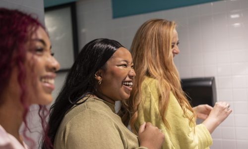Three diverse young women smiling and laughing together, fostering connection and positivity in the workplace.