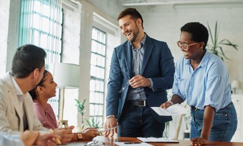 A group of coworkers smiling and collaborating during a team meeting, reflecting a positive, high-trust workplace culture that supports strong startup valuation.